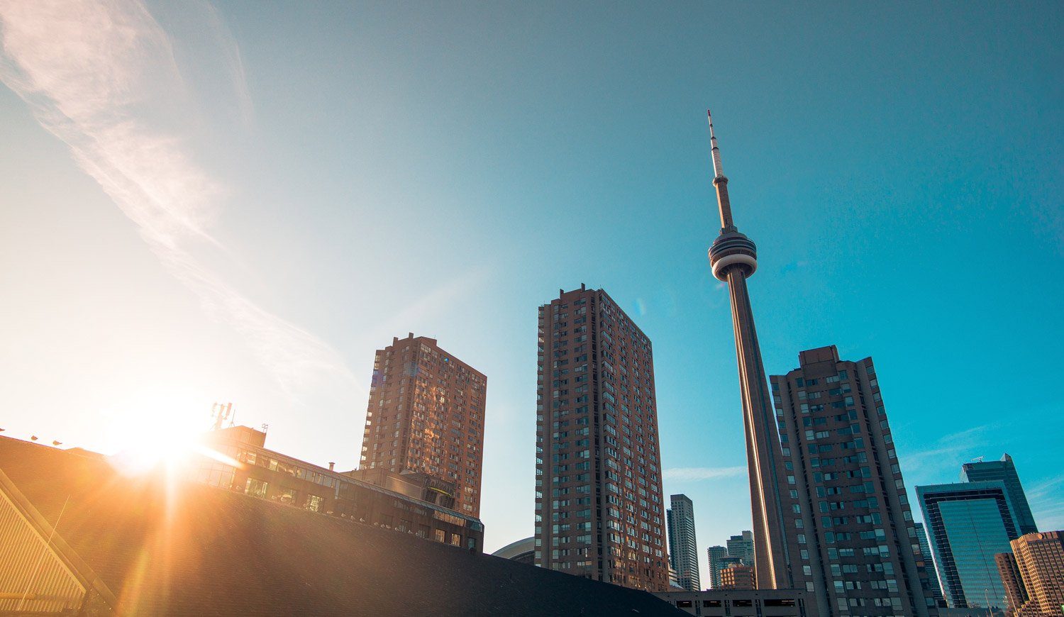 The CN Tower sits in between 2 tall brown buildings to the left and one tall brown building to the right.