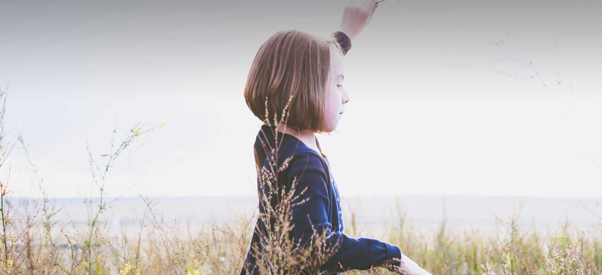 Young girl holds left hand high while looking down in a field