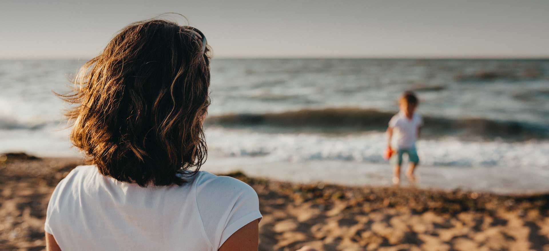 Woman watches young boy play on shoreline of beach