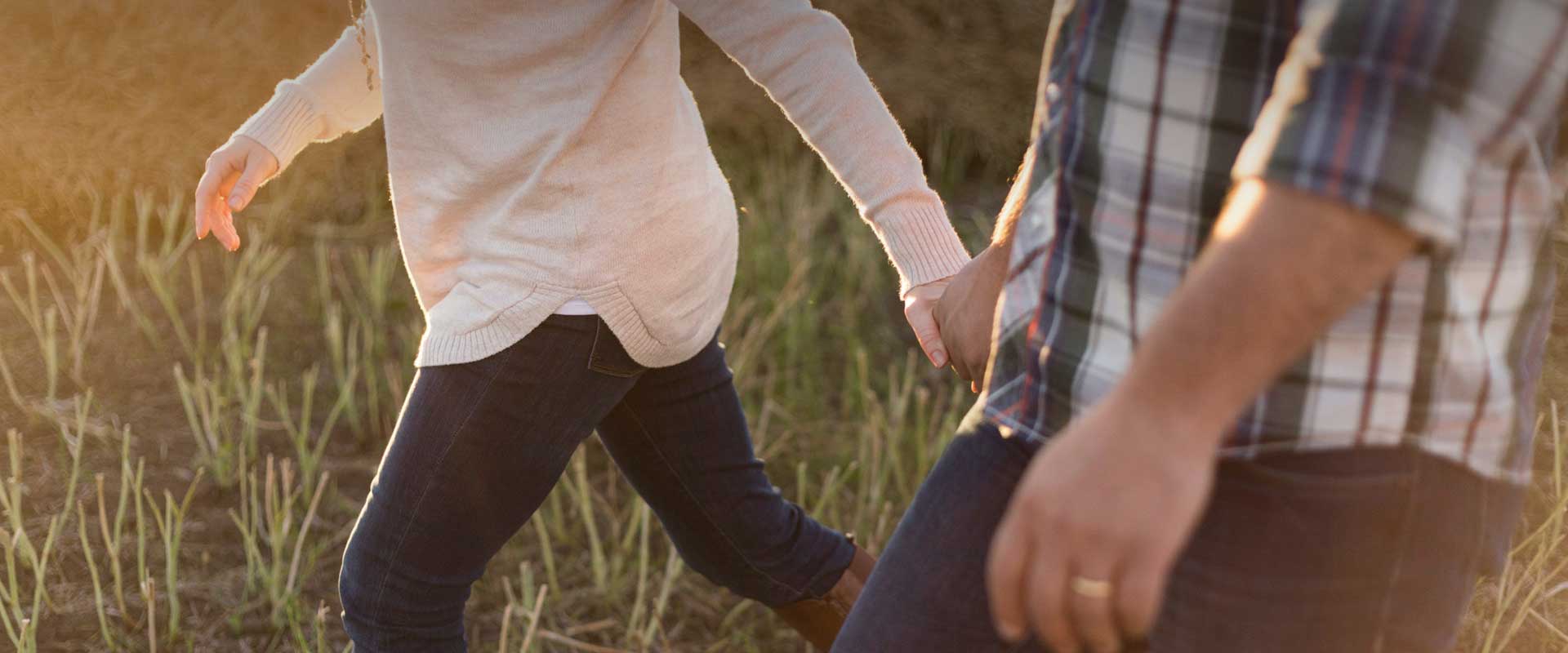 A married man and a woman hold hands while walking through the grass.